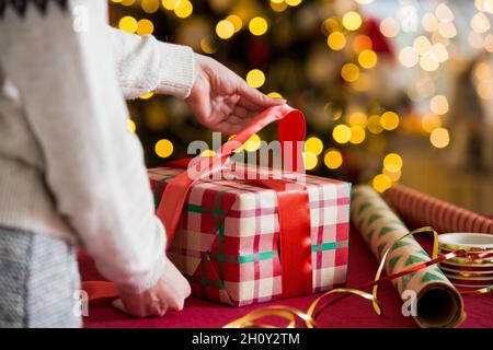 Mann und Frau bereiten sich auf Weihnachten vor. Pairle in warme Pullover Geschenkverpackung. Geschmückter Weihnachtsbaum, Schachteln mit Geschenken, buntes Geschenkpapier Stockfoto