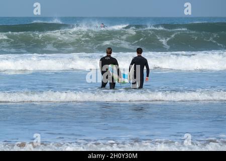 Zwei Surfer gehen an einem Oktobertag in Putsborough, North Devon, Großbritannien, in die Wellen. Stockfoto