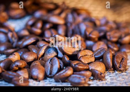 Nahaufnahme von frisch gerösteten Kaffeebohnen, die bei gemischtem Licht aus einem Jutesack mit geringer Schärfentiefe gestreut wurden. Stockfoto