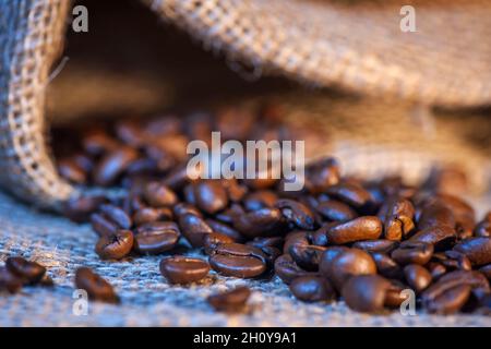 Nahaufnahme von frisch gerösteten Kaffeebohnen, die aus einem Sackleinen gestreut wurden. Stockfoto