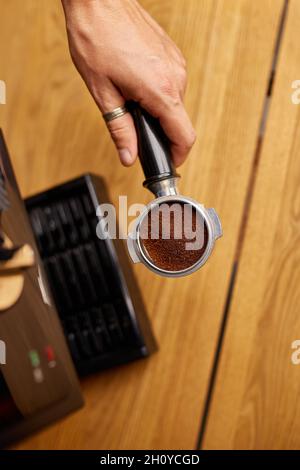 Weibliche Hände halten Portafilter und machen frischen aromatischen Kaffee zu Hause mit einer modernen Kaffeemaschine, männliche Barista Hand Espresso aus gemahlenem c Stockfoto