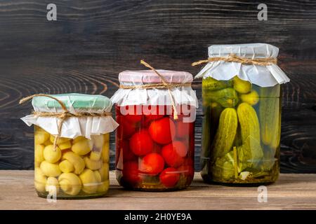 Hausgemachte eingelegte Kirschtomaten, Gurken, Champignons, Knoblauch, Auberginen, Rote Paprika in Gläsern auf Holzregal hausgemachte Konserven und fermentierte Lebensmittel CO Stockfoto