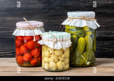 Hausgemachte eingelegte Kirschtomaten, Gurken, Champignons, Knoblauch, Auberginen, Rote Paprika in Gläsern auf Holzregal hausgemachte Konserven und fermentierte Lebensmittel CO Stockfoto