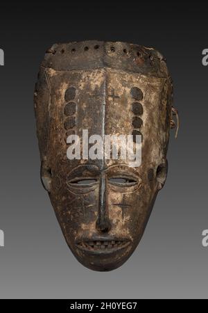 Gesichtsmaske (Iru mmuo), möglicherweise Anfang des 20. Jahrhunderts. Guinea Coast, Nigeria, Igbo Menschen. Holz, Pigment, Pflanzenfasern und Baumwolle; insgesamt 16.9 x 11 x 6 cm (6 5/8 x 4 5/16 x 2 3/8 Zoll). Diese kleine Gesichtsmaske wäre durch einen separaten, aufwändigen Überbau mit Baumwolltuch überzogen worden. Obwohl das Bild immer von einem Mann getragen wird, verherrlicht es die Jugendliche weibliche Schönheit. Die weiße Färbung des Gesichts, abgeleitet aus kalkhaltigen Tonerden, bezieht sich auf uralte Geister, deren Kräfte die Maske hervorruft. Die Masken tanzen auf Festen, die in der Regel die Toten feiern, aber auch auf Beerdigungen erscheinen, um die Verstorbenen zu eskortieren Stockfoto