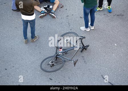 Fahrradunfall auf der Straße. Szene von Radler und Fahrrad auf dem Asphalt, umgeben von Menschen, nachdem sie von einem Fahrzeug getroffen wurden Stockfoto