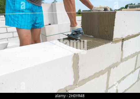 Der Baumeister verwendet eine gekerbte Kelle, um das Zementgemisch aus nächster Nähe auf die belüftelten Betonblöcke aufzutragen. Konzept des Aufbaus eines Privathauses Stockfoto