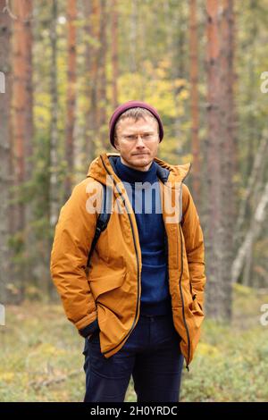 Mittelalter bärtiger kaukasischer Mann mit Rucksack, der über dem Waldhintergrund steht.Reisender, der im Herbstwald spaziert - Bild Stockfoto