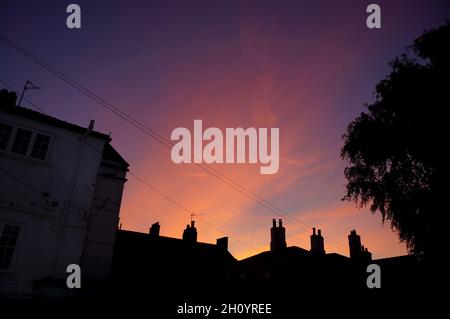 Atemberaubender orange-rosafarbener Sonnenuntergang über alten Hausdächern im Herbst Stockfoto