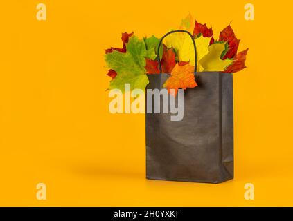 Herbstblätter in einer Tasche auf orangefarbenem Hintergrund. Saisonale Komposition für Layouts, Vorlage mit Ort für Text. Konzept - Herbstangebot, Shopping-Trip. Stockfoto