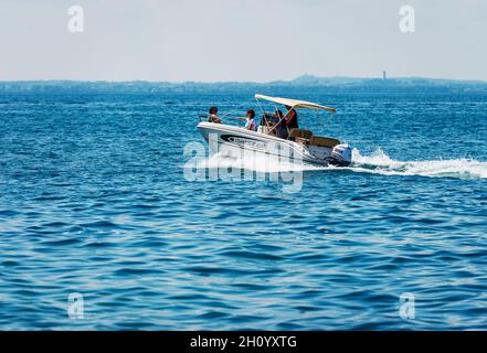 Kleines Mietboot mit einer Familie an Bord in Bewegung am Gardasee. Bardolino Dorf, Ferienort in der Provinz Verona, Venetien, Italien, Europa. Stockfoto