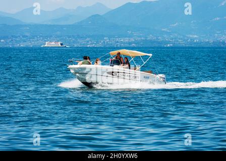 Kleines Mietboot mit einer Familie an Bord in Bewegung am Gardasee. Bardolino Dorf, Ferienort in der Provinz Verona, Venetien, Italien, Europa. Stockfoto