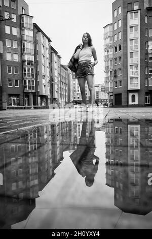 Mädchen in der Nähe Herbst Pfütze mit Reflexionen auf Stadtplatz, monochrom Stockfoto