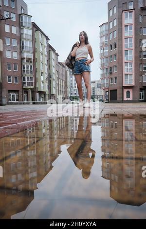 Mädchen in der Nähe Herbst Pfütze mit Reflexionen auf dem Stadtplatz Stockfoto