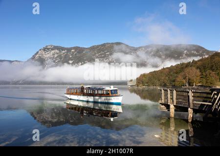 Bohinj, Slowenien. Oktober 2021. Der Nebel über dem Bohinjer See zerstreut sich in der Morgensonne und die Berge werden sichtbar, wenn ein Boot am Anlegesteg ankommt. Quelle: Jürgen Schwarz/Alamy Live News Stockfoto