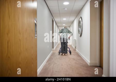 Rückansicht Einer Älteren Frau Mit Walker, Die Im Altersheim Den Korridor Entlang Läuft Stockfoto