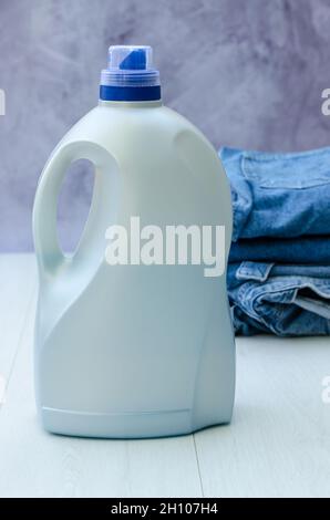 Eine Flasche flüssiges Pulver im Vordergrund und ein Stapel Dinge im Hintergrund. Waschmittel zum Waschen. Stockfoto