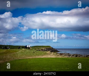 HAFNARFJORDUR, ISLAND - 31. Mai 2021: Golfspieler ruhen sich auf einer Bank mit Meerblick auf einem grünen Golfplatz in Hafnarfjordur aus. Stockfoto