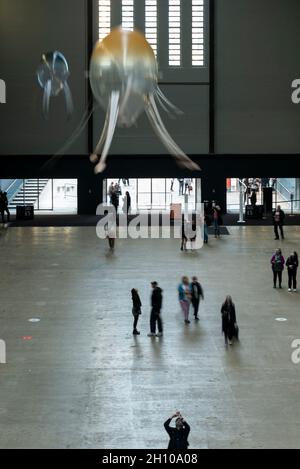 London, Großbritannien. Oktober 2021. Die Besucher sehen schwebende Kunstflugkörper, die Anicka Yis neues Luftwerk „in Love With The World“ bilden, in der Turbine Hall of Tate Modern für die Hyundai-Kommission 2021. Die Installation besteht aus Maschinen, die als Kunstflugkörper bezeichnet werden, basierend auf Lebensformen des Ozeans und Pilzen, die in der Luft schweben, und stellt eine Neueinbildung dar, wie künstliche Intelligenz und neue Maschinen die Welt bewohnen könnten. Die Arbeit kann bis zum 16. Januar 2022 erlebt werden. (Langzeitbelichtung). Kredit: Stephen Chung/Alamy Live Nachrichten Stockfoto