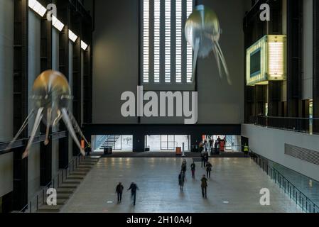 London, Großbritannien. Oktober 2021. Die Besucher sehen schwebende Kunstflugkörper, die Anicka Yis neues Luftwerk „in Love With The World“ bilden, in der Turbine Hall of Tate Modern für die Hyundai-Kommission 2021. Die Installation besteht aus Maschinen, die als Kunstflugkörper bezeichnet werden, basierend auf Lebensformen des Ozeans und Pilzen, die in der Luft schweben, und stellt eine Neueinbildung dar, wie künstliche Intelligenz und neue Maschinen die Welt bewohnen könnten. Die Arbeit kann bis zum 16. Januar 2022 erlebt werden. (Langzeitbelichtung). Kredit: Stephen Chung/Alamy Live Nachrichten Stockfoto