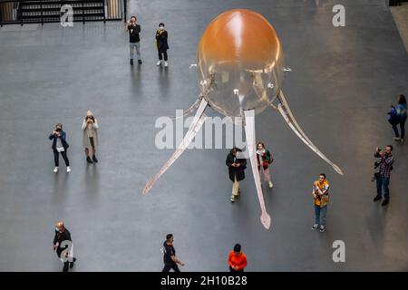 London, Großbritannien. 15. Oktober 2021. Die Besucher sehen schwebende Kunstflugkörper, die Anicka Yis neues Luftwerk „in Love With The World“ bilden, in der Turbine Hall of Tate Modern für die Hyundai-Kommission 2021. Die Installation besteht aus Maschinen, die als Kunstflugkörper bezeichnet werden, basierend auf Lebensformen des Ozeans und Pilzen, die in der Luft schweben, und stellt eine Neueinbildung dar, wie künstliche Intelligenz und neue Maschinen die Welt bewohnen könnten. Die Arbeit kann bis zum 16. Januar 2022 erlebt werden. Kredit: Stephen Chung / Alamy Live Nachrichten Stockfoto