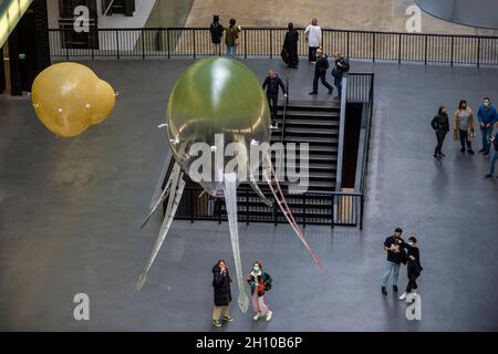 London, Großbritannien. 15. Oktober 2021. Die Besucher sehen schwebende Kunstflugkörper, die Anicka Yis neues Luftwerk „in Love With The World“ bilden, in der Turbine Hall of Tate Modern für die Hyundai-Kommission 2021. Die Installation besteht aus Maschinen, die als Kunstflugkörper bezeichnet werden, basierend auf Lebensformen des Ozeans und Pilzen, die in der Luft schweben, und stellt eine Neueinbildung dar, wie künstliche Intelligenz und neue Maschinen die Welt bewohnen könnten. Die Arbeit kann bis zum 16. Januar 2022 erlebt werden. Kredit: Stephen Chung / Alamy Live Nachrichten Stockfoto