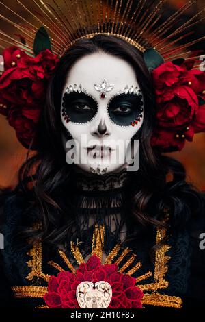 Porträt einer jungen Frau mit Totenschädel-Make-up und roten Rosen in schwarzem Todeskostüm als Santa Muerte. Tag der Toten oder Halloween-Konzept. Stockfoto