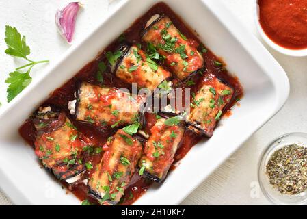 Nahaufnahme von gebackenen gefüllten Auberginen-Brötchen mit Tomatensauce in Backform auf weißem Hintergrund. Draufsicht, flach liegend Stockfoto