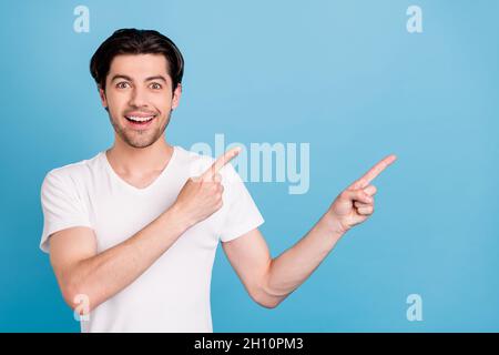 Foto von lustig froh Kerl zeigen Zeigefinger leeren Raum Verkauf Banner tragen weißes T-Shirt isoliert blauen Hintergrund Stockfoto