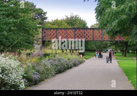 Burgess Park, Peckham, London, Großbritannien. Radfahrer und Fußgänger auf einem Weg entlang der alten Surrey Canal Route. Zeigt die originale viktorianische Kanalbrücke. Stockfoto