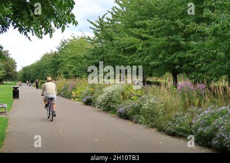 Burgess Park, Peckham, London, Großbritannien. Radfahrer und Fußgänger auf einem Weg entlang der alten Surrey Canal Route. Zeigt die originale viktorianische Kanalbrücke. Stockfoto