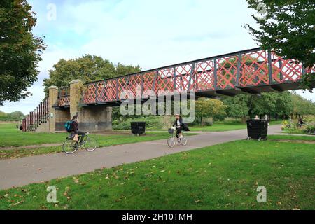 Burgess Park, Peckham, London, Großbritannien. Radfahrer und Fußgänger auf einem Weg entlang der alten Surrey Canal Route. Zeigt die originale viktorianische Kanalbrücke. Stockfoto