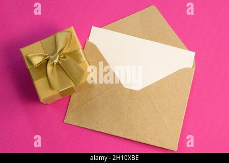 Einfacher kleiner Umschlag mit Platz zum Schreiben und niedlicher kleiner Rose auf Holzhintergrund mit goldener Geschenkbox close-up schmale Fokuslinie, geringe Tiefe von Stockfoto