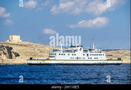 Eine Fähre auf dem Weg von Malta nach Gozo fährt an der St. Marias Turm. Der 1618 erbaute Bastionsturm, auch Comino Tower genannt, befindet sich auf den steilen Klippen von Comino und kontrolliert den Gozo-Kanal, die Meerenge zwischen den Inseln Malta und Gozo. Stockfoto