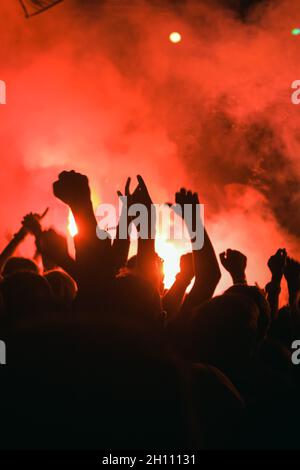 Silhouetten von Menschen gegen das rote Licht der Fackel vor der Bühne bei einem Musikrock-Festival. Eine Menge Fans bei einem Konzert Stockfoto