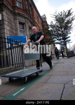 Grüne Linie als Leitfaden für Sehbehinderte an der Außenseite der Moorfields. Das Moorfields Eye Hospital ist ein spezialisiertes NHS-Augenkrankenhaus in Islington London, England, das vom Moorfields Eye Hospital NHS Foundation Trust betrieben wird und von dem ein Mann den Trolley entlang der Straße schiebt Stockfoto