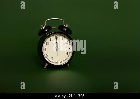 Studio-Aufnahme mit weichen Schatten eines schwarzen Weckers mit Mitternacht auf dem Ziffernblatt isoliert auf dunkelgrünem Hintergrund mit Kopierfläche für Werbung. Zeit Stockfoto