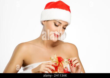 Schöne junge Frau in einem festlichen roten Weihnachtsmann Hut mit gepflegten Nägeln Auspacken al Weihnachtsgeschenk mit einem glückseligen Lächeln, als sie den Feiertag feiert Stockfoto