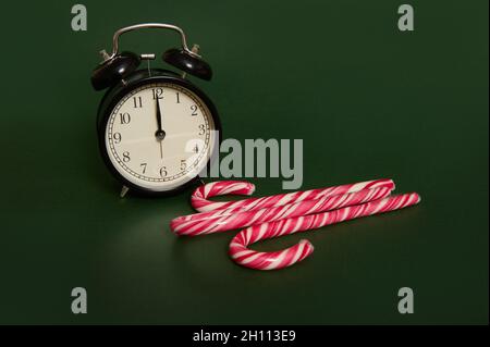 Das Studio wurde mit Schatten eines schwarzen Weckers mit Mitternacht auf dem Zifferblatt und zuckersüßen gestreiften Weihnachtslutschern aufgenommen, die über Dunkelheit isoliert wurden Stockfoto