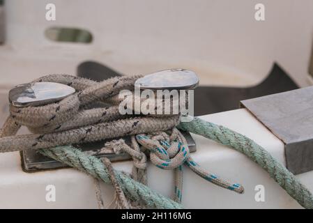 Schiffsbollard mit grünen und grauen Seilen, an denen ein blaues Boot festgemacht ist Stockfoto