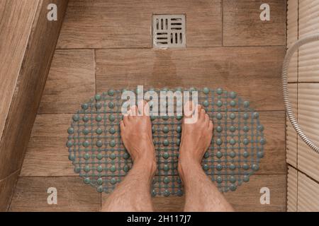Herrenfüße stehen auf einer rutschfesten Kunststoffmatte neben dem Bodenablauf im Bad oder in der Dusche. Stockfoto