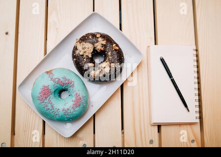 Draufsicht von leckeren Donuts auf einer weißen rechteckigen Platte neben einem Notizbuch und einem Kugelschreiber Stockfoto