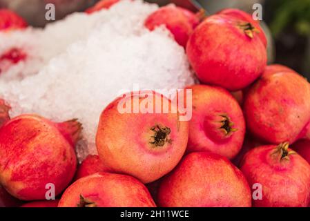 Granatäpfel liegen auf einem Marktstand. Rote Granatapfelfrüchte und Eis, um sie frisch zu halten. Stockfoto