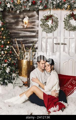 Model junge Frau und ihr gutaussehender Freund posiert im Winter rustikalen Interieur für Neujahr mit künstlichem Schnee und Weihnachtsbaum dekoriert Stockfoto