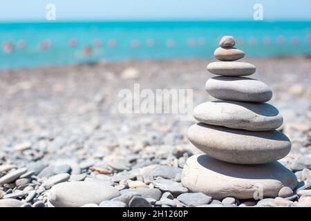 An einem sonnigen Tag werden runde Steine übereinander in einer Pyramide an der Küste gestapelt. Balance-Konzept. Speicherplatz kopieren. Stockfoto