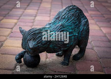 Trzebnica, Polen - 29. August 2021: Bronzeskulptur einer Katze „Zdrojek“, die mit einem Ball auf dem Gehweg vor einer Sporthalle spielt. Stockfoto