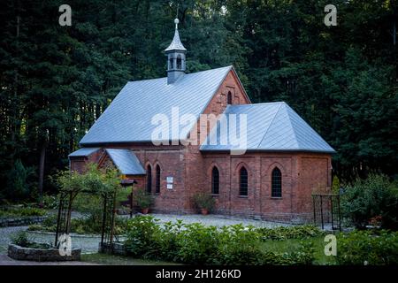 Trzebnica, Polen - 29. August 2021: Eine neogotische Backsteinkirche der vierzehn Heiligen Helfer, umgeben vom Wald. Stockfoto