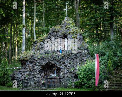Trzebnica, Polen - 29. August 2021: Eine Steinhöhle mit Altar der Heiligen Maria, umgeben von Wald, vor einer Kirche der vierzehn Heiligen Helfer. Stockfoto