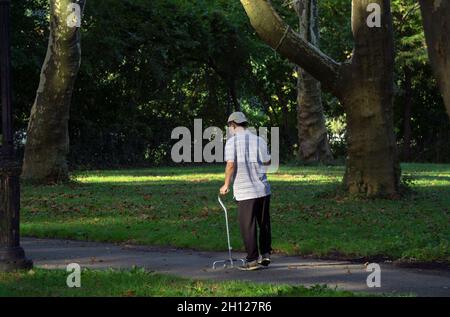 Ein älterer Mann, der mit einem vierbeinigen Stock auf einem malerischen Pfad läuft. In einem Park in Queens New York an einem sonnigen Herbsttag. Stockfoto