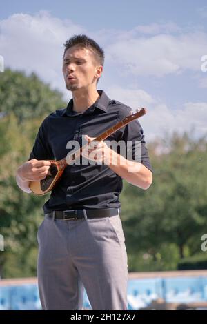 Ein junger Mann aus Montenegro spielt bei einem Fotoshooting in einem Park in Queens, New York City, eine cifteli 2-saitige Gitarre. Stockfoto