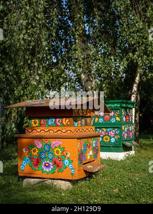 Zalipie, Polen - 1. August 2021: Zwei bunte Bienenstöcke aus Holz im Garten, mit Blumenmuster bemalt. Sonniger Sommertag. Stockfoto